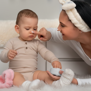 Woman applying cream to a baby's nose in a cozy setting